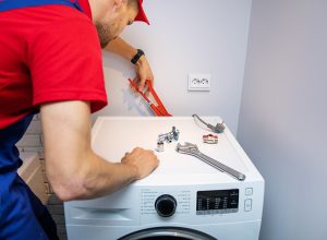 A laundromatic handy man bending over installing a washing appliance, which is one of Laundromatic's convenient services.